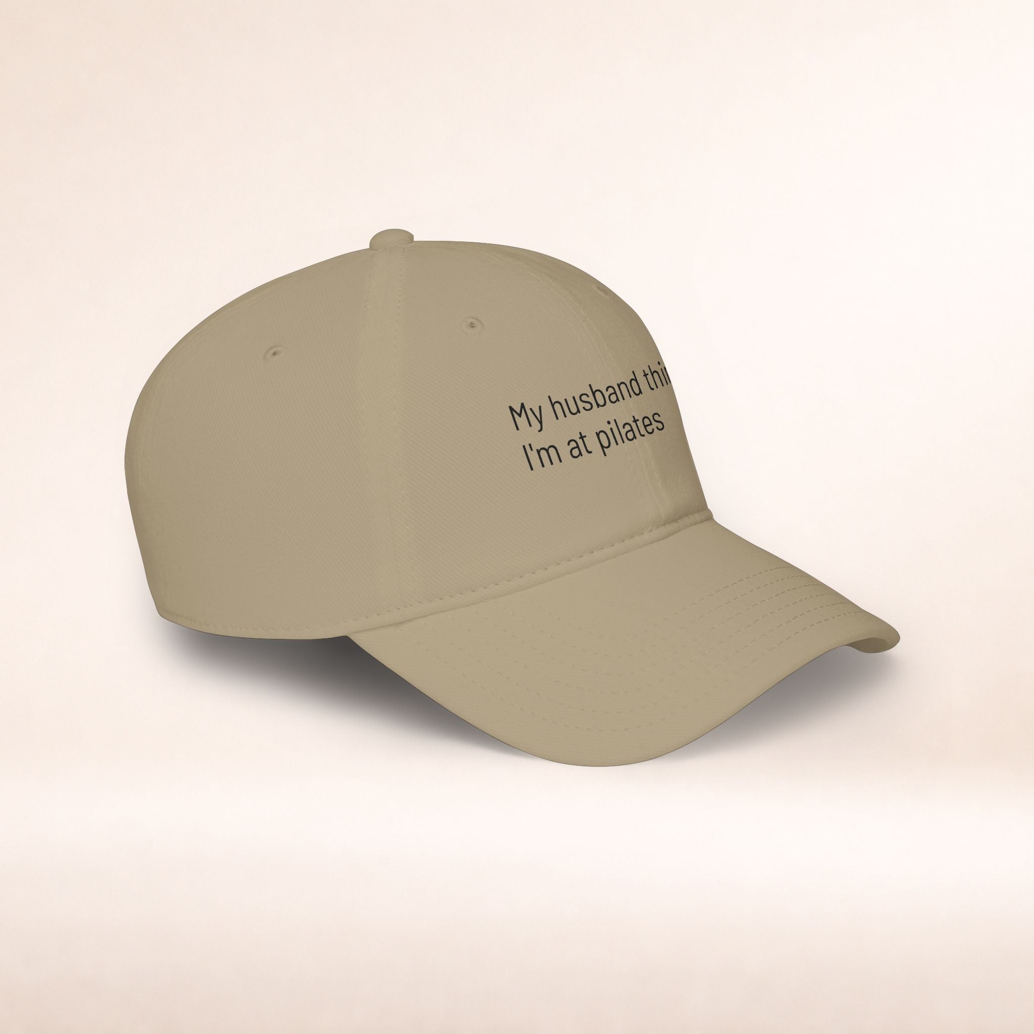 Black low profile baseball cap with embroidered text "My Husband Thinks I'm At Pilates" by Printify, casual hat with humorous design.