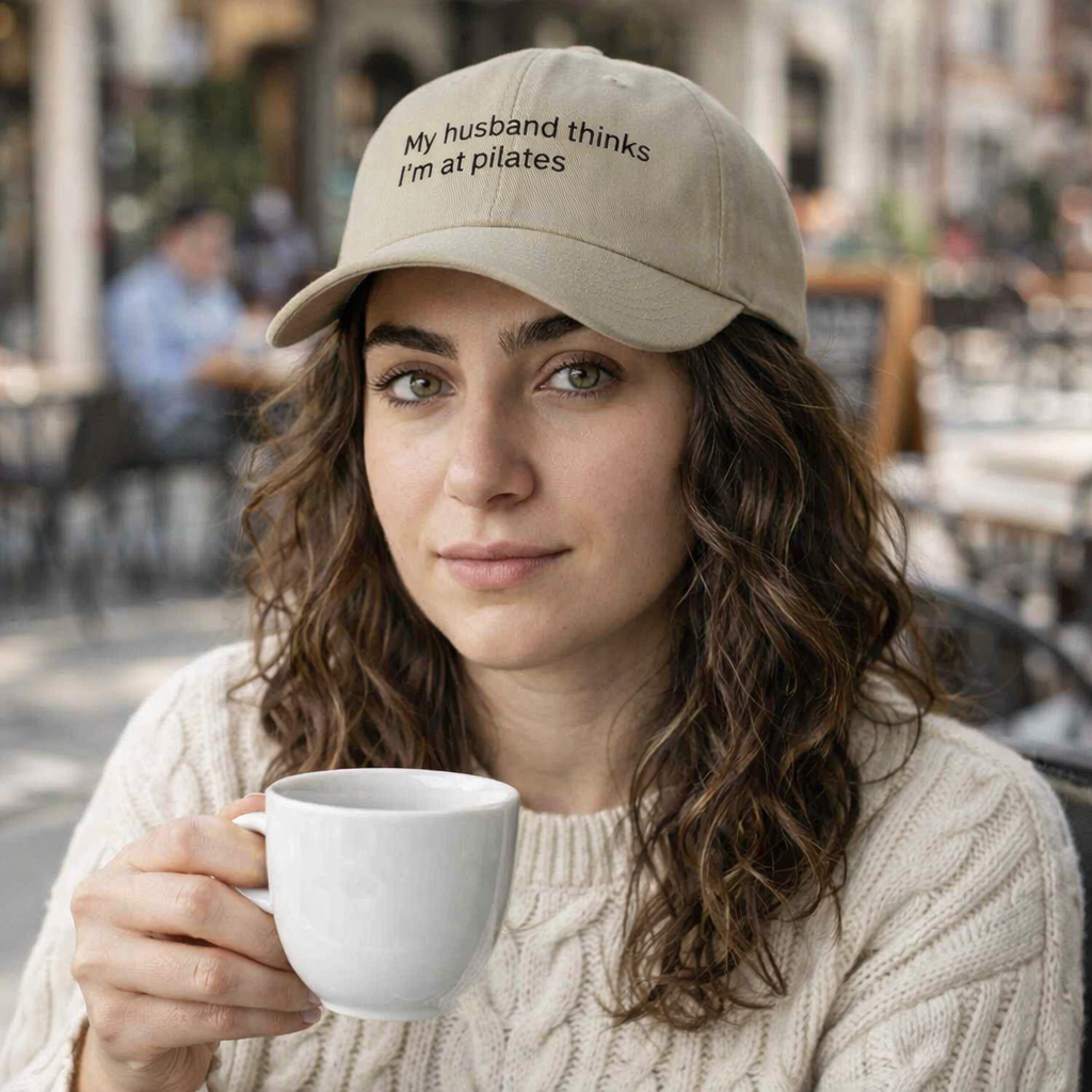 Black low-profile baseball cap with embroidered text "My Husband Thinks I'm At Pilates" by Printify, featuring a casual, stylish design.